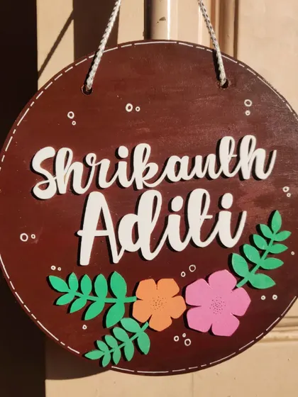 A floral-themed couple's nameplate with a rich, dark wood finish. The colorful flowers and leaves add a touch of nature and warmth, making it a lovely piece for any home entrance.
