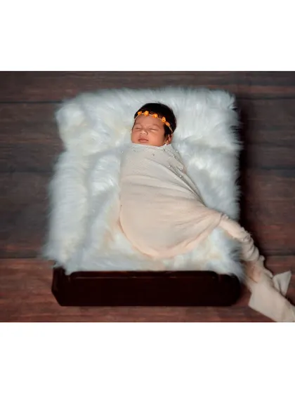 A newborn swaddled and sleeping on a miniature bed with a white fur blanket.