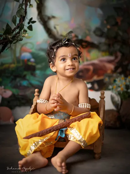 A magical moment with a little Krishna sitting on a tiny wooden bed in our enchanted forest. His curious expression as he looks up creates a storybook-like image.