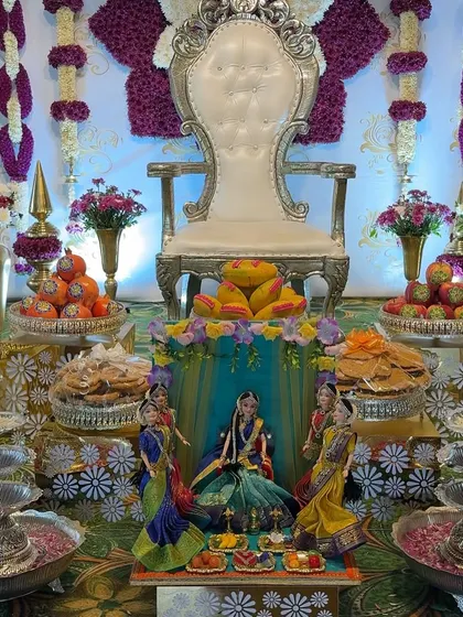 A close-up of a baby shower decoration, highlighting the intricate plate arrangements. You can see the variety of sweets and fruits, along with a central doll scene, all set against a purple and white floral theme.