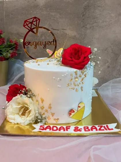 Every detail tells a love story. This engagement cake is decorated with red and white roses, gold leaf, and a custom name banner for Sadaf and Bazil.