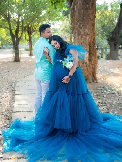 A tender moment between a couple during their outdoor shoot. The mom-to-be, in a royal blue gown, rests her head on her partner's shoulder.