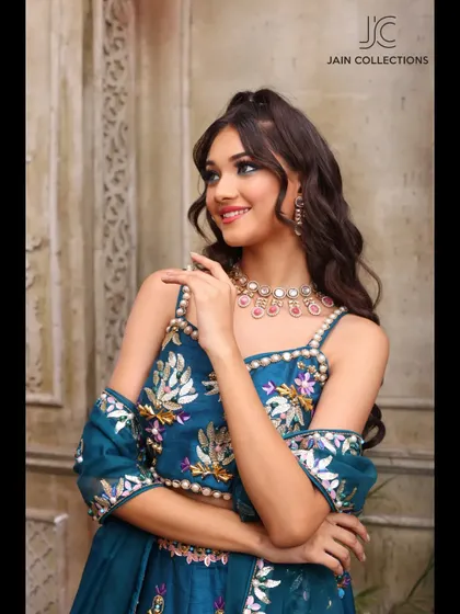 Another smiling shot of a model in the teal floral lehenga, showcasing its off-shoulder blouse design and vibrant colors.