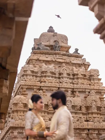 A slightly out-of-focus foreground of the temple pillars creates a sense of depth, drawing the viewer's eye to the couple sharing a look in front of the magnificent temple structure.