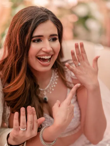 The bride excitedly shows off her and her new fiancé's rings to the camera, a moment of pure happiness.