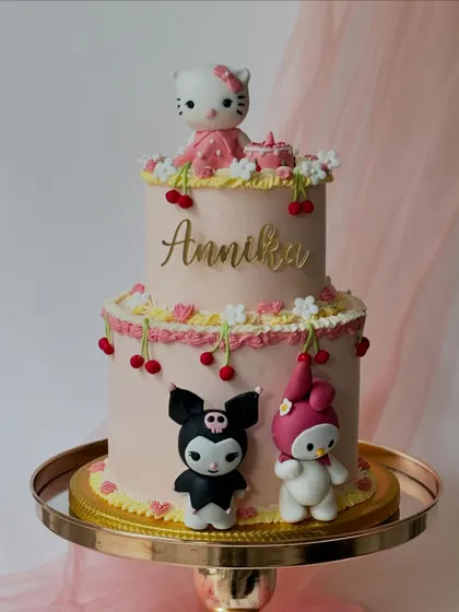 A Sanrio-themed cake featuring Hello Kitty, Kuromi, and My Melody. This two-tiered design is decorated with delicate buttercream piping and fondant cherries for a cute and detailed look.