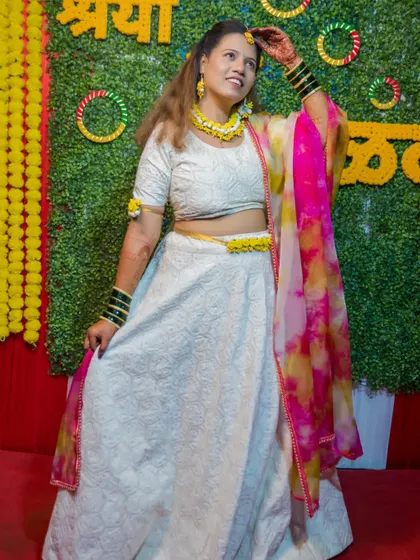 The bride shows off her full Haldi outfit, a beautiful white lehenga complemented by a colorful dupatta and floral accessories.