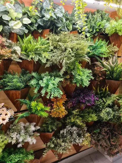 A display of various artificial plants in triangular wall-mounted planters, showcasing the different types of foliage available for low-maintenance vertical gardens.