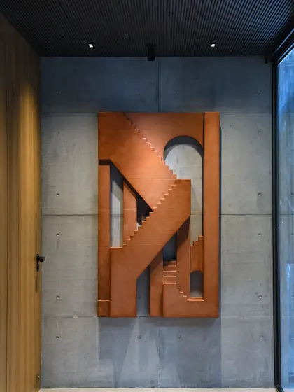The Swatantra Residence is a visual fusion of art and architecture. This bespoke wooden artwork, resembling a series of staircases, is mounted on a raw concrete wall, transforming the space into a dynamic exhibition.