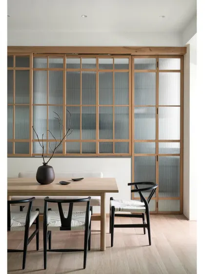 In this dining area, a white oak table is paired with black open-grain wishbone chairs. Versatile wooden sliding doors with fluted glass create a perfect harmony between an open and closed kitchen experience.