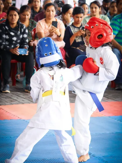 Two of our young female students engage in a controlled kumite (sparring) match during a championship. Dressed in full protective gear, including head guards and gloves, they demonstrate proper technique and sportsmanship, highlighting our focus on safe and practical self-defense training for girls and boys.