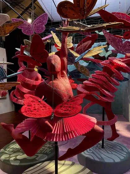 The 'We/Us' installation features multiple dancing figures in a cloud of butterflies. The entire scene is a dynamic and bold expression of liberation, confidence, and the joy of uninhibited movement.