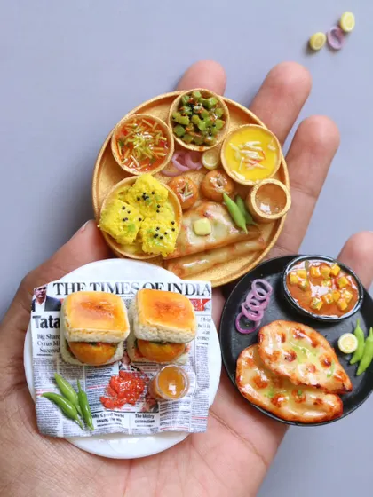 A collection of miniatures featuring vada pav, naan with curry, and a Kathiawadi thali, held in hand to show their scale.