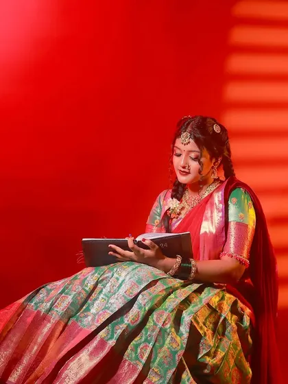 A model in a traditional half-saree, reading a book under dramatic red lighting, creating an artistic and cultural portrait.