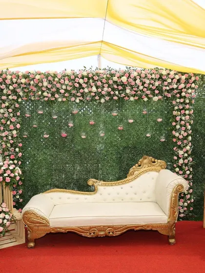 The main photo booth area for a small wedding, featuring a beautiful chaise lounge against a wall of greenery and flowers. It's a perfect spot for capturing special moments.