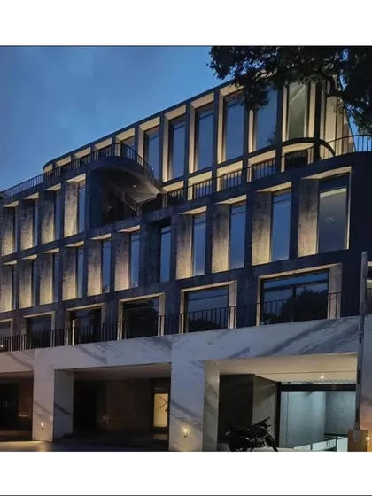 The completed office building at night. The facade is illuminated with uplighting, highlighting the texture of the stone and the rhythmic pattern of the windows.