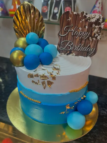 A custom cake with a blue and gold theme. The design features blue ombre frosting, golden spheres, and a "Happy Birthday" message for Mr. Gade, creating a regal and celebratory look.