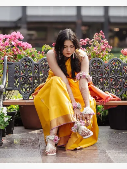 A portrait of the bride sitting on a bench surrounded by flowers at her Haldi in Siliguri.