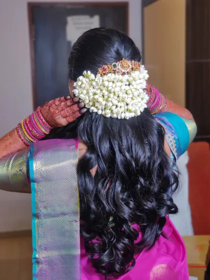 The back of her hairstyle, featuring a beautiful bun adorned with fresh jasmine and a traditional hair accessory.