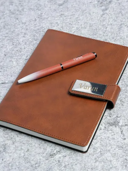 A close-up of a tan diary and pen set, personalized with the name "Varun" on both the metal plate and the pen.