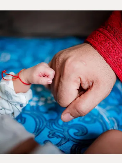 A baby's fist bump with their father, a modern and sweet take on the parent-child bond captured during a traditional ceremony.