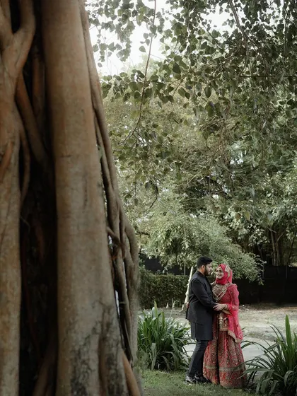 A romantic, wide-angle shot of the bride and groom under a large tree, emphasizing the scale and beauty of nature surrounding them.