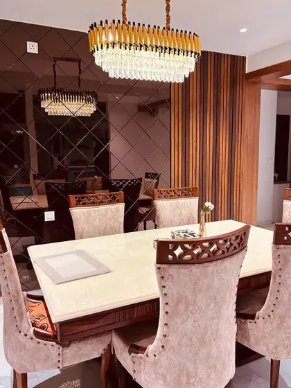 An elegant dining area designed for memorable gatherings. The space is defined by a stunning crystal chandelier, a reflective smoked-glass wall that enhances the sense of space, and luxurious upholstered chairs for ultimate comfort.