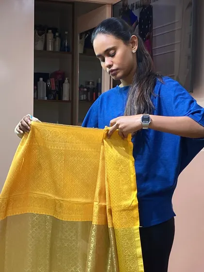 A student practices pre-pleating a silk saree, a crucial skill for achieving a neat and professional drape, especially for bridal events.
