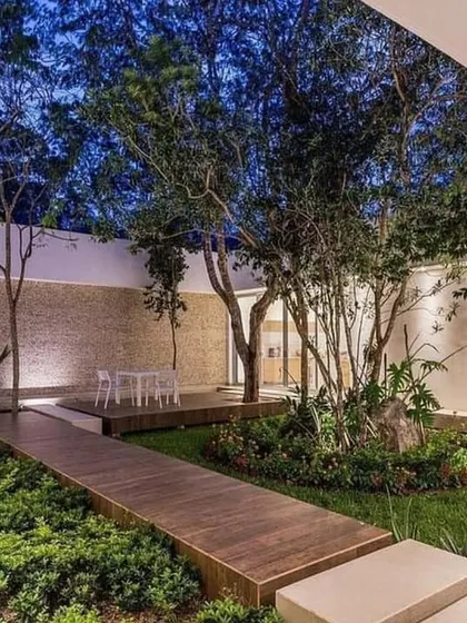 An open-roof courtyard at twilight, where our lighting design creates a magical atmosphere. The uplighting on the trees and the wooden deck walkway make this central garden a usable and beautiful space day and night.