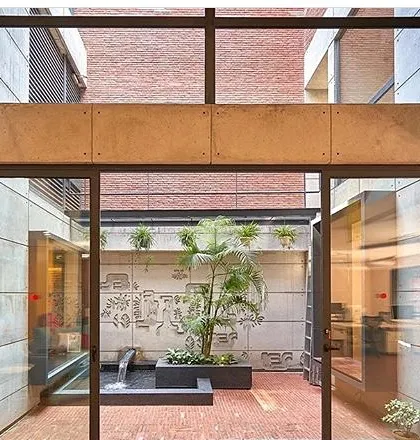 A concept render for an indoor courtyard. The design includes a central planter with a palm tree, a small water feature, and wall carvings, creating a serene internal view.