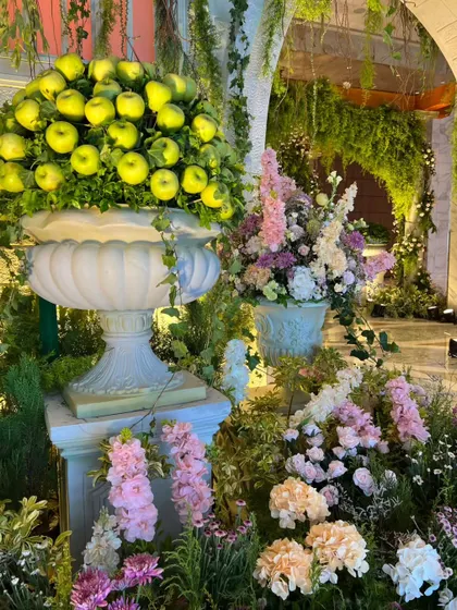 A unique floral installation combining a large urn filled with green apples and another with pastel-colored flowers, adding a touch of rustic Italian charm.