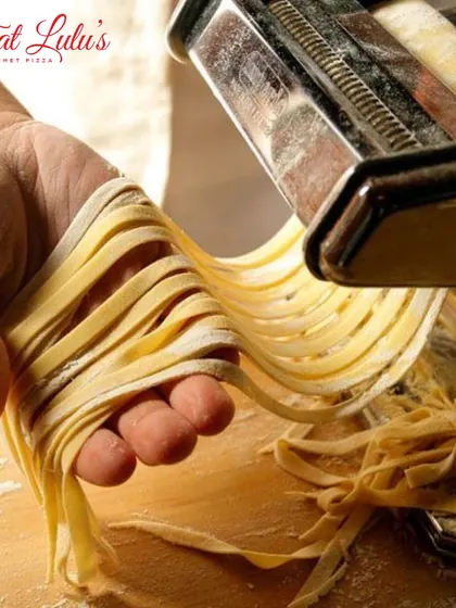 A close-up of a chef's hand guiding freshly cut fettuccine as it comes through the pasta machine. This is a key technique for making long pasta shapes.