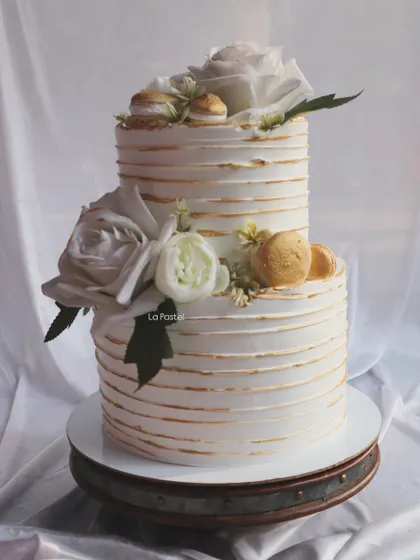 A beautiful two-tier cake with white and gold line details. I decorated it with white roses and macarons for a chic and sophisticated celebration.