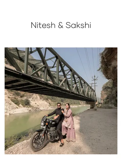A classic portrait of the couple with their motorcycle by the river, set against the impressive structure of a bridge in Rishikesh.