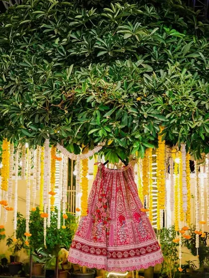 A creative shot of the bride's pink lehenga hanging from a beautifully decorated tree. This unique display turns the wedding dress into a piece of art within the decor.