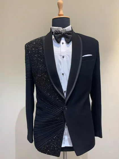 This mannequin showcases a jet-black tuxedo with an asymmetrical design. One side features heavy sequin and bead work with fabric ruching, while the other remains classic, offering a modern twist on formal wear.