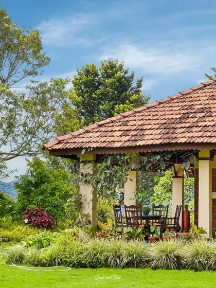 The exterior of Villa Magnolia in Virajpet, a traditional home with a tiled roof and a sprawling veranda. The lush garden and manicured lawn create a serene and picturesque setting.