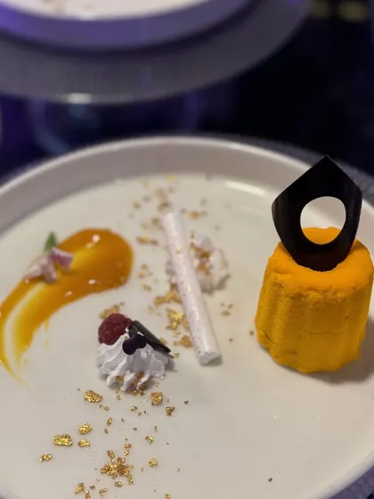 A modern dessert composition. A vibrant yellow mousse is adorned with a sculptural chocolate piece and delicate meringue, demonstrating our pastry team's skill in creating designer desserts.