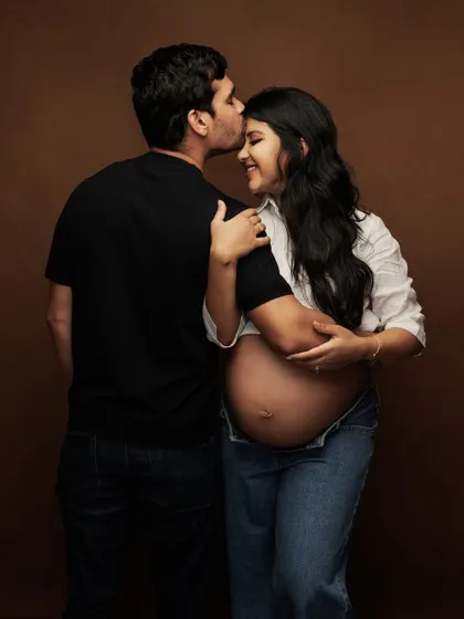 A tender moment captured during a casual studio maternity session. The father-to-be kisses his partner's forehead, a simple gesture of love and support.