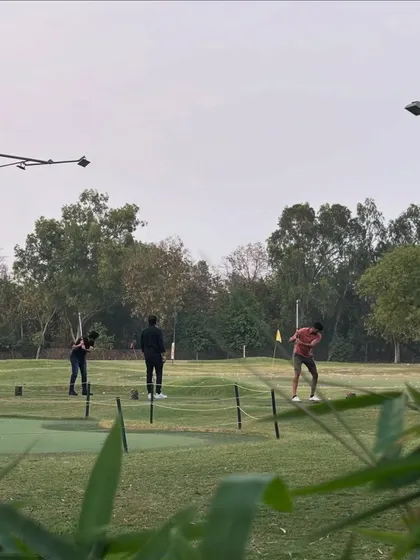A view of the putting green through the foliage, where golfers are honing their short game.