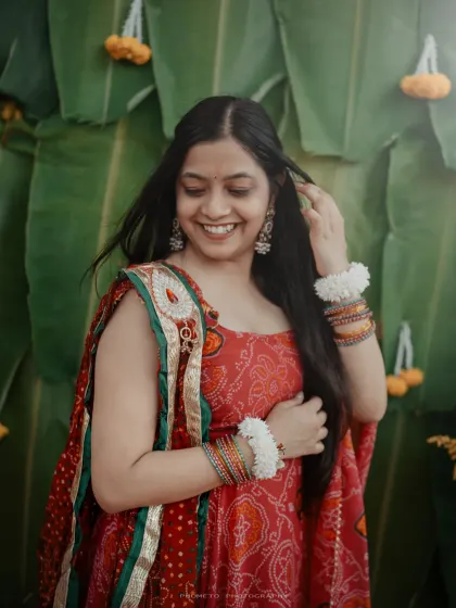 A joyful bride during her Haldi ceremony, her red and green outfit a beautiful contrast against the banana leaf backdrop.