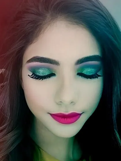 This look features a vibrant green and purple cut crease eyeshadow, paired with dramatic false lashes and a bright pink lip. It's a bold and artistic choice for someone looking to make an impact at a party or special event.