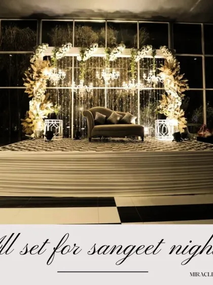A glamorous white and gold stage setup for a Sangeet or engagement. The cascading crystals and floral arch create a look of pure elegance.