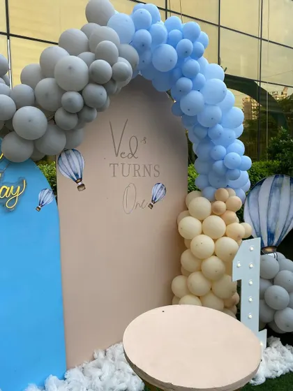 A close-up of the hot air balloon theme for Ved's first birthday, with a custom backdrop, marquee number, and a soft color palette of blue, grey, and beige.