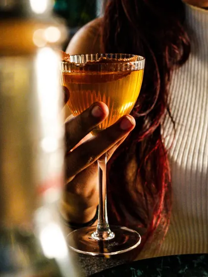 A beautifully composed shot of a woman holding a classic cocktail. The warm, golden hour lighting creates a sophisticated and relaxed atmosphere.