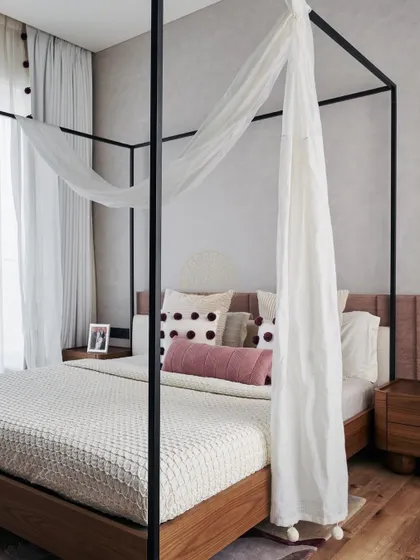 This master bedroom in a 4500 sq ft Mumbai home features a classic four-poster bed draped with sheer white fabric, creating a romantic and dreamy atmosphere. The color palette is soft and neutral, with pops of pink.