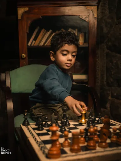 A young boy, deep in thought, makes his move on the chessboard. This moody, atmospheric shot captures a moment of quiet concentration.