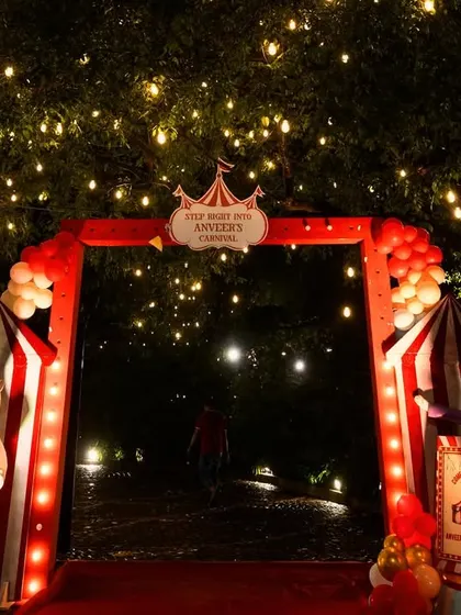 The entrance to a carnival-themed party at night. The archway is decorated with red-and-white striped tents and lit with string lights, creating a magical and inviting ambiance.