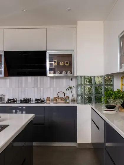 A wider view of the industrial-transitional kitchen, showing the U-shaped layout. The design features a mix of glossy white and grey cabinets, a white subway tile backsplash, and a glass block window for added light.