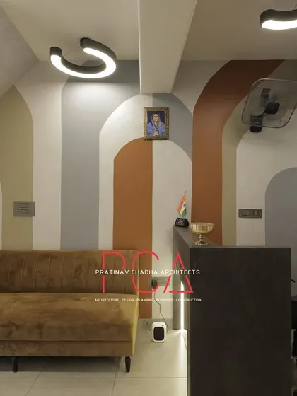 The waiting area at StyleIn Homes, featuring a comfortable sofa set against a wall with modern, arched color blocking and a textured 3D panel.